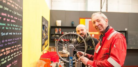 two men smiling into the camera working on bike tyres in a workshop