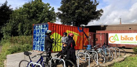 the Bike for Good Civic Street cycling hub - a shipping container bright and colourful with lots of bikes outside. There are three people chatting