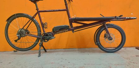 Side view of an Omnium cargo bike against an orange background.