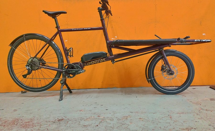 Side view of an Omnium cargo bike against an orange background.